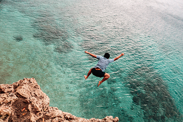 Jongen springt van een rots in de zee